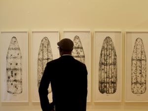 man dressed in black looks at five rectangular art pieces