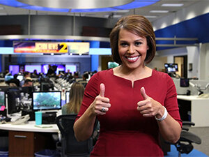 Jovita in the newsroom giving a thumbs-up to the camera 
