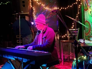 Man with striped hat playing a keyboard piano under purple light