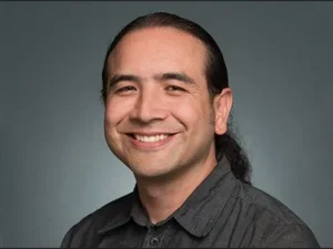 Smiling man in grey shirt with pony tail on smooth grey background