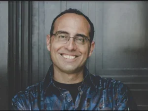 smiling man in blue shirt in front of a grey door