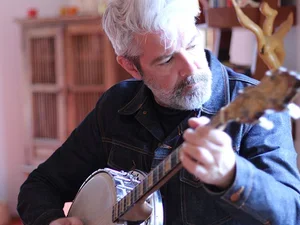 An older white man with a short grey beard playing banjo