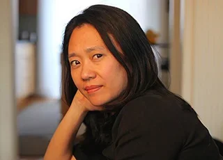 woman with dark hair wearing a black top gazes into camera lens 