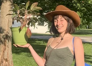 Photo of Jack de Loos; woman in green tank top, brown cowboy hat, holding plant