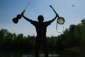 silhouette of man holding fiddle and banjo at dusk