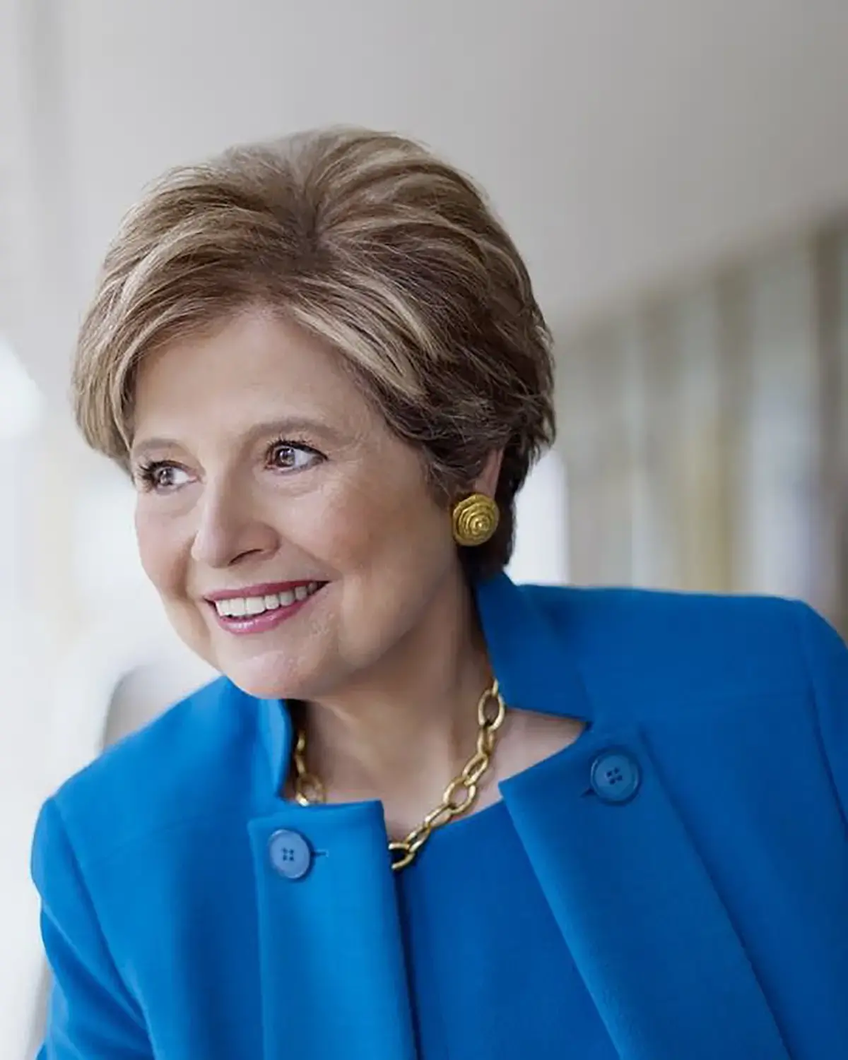 Woman with short blonde hair and blue suit smiling, with white background